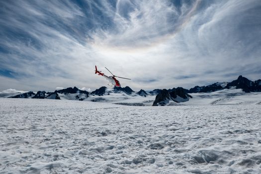 A helicopter hovers over a stunning snowy landscape in New Zealand with dramatic skies.