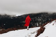 一个身穿鲜红外套的人，正沿着白雪皑皑的山间小路行走，四周雾气弥漫
