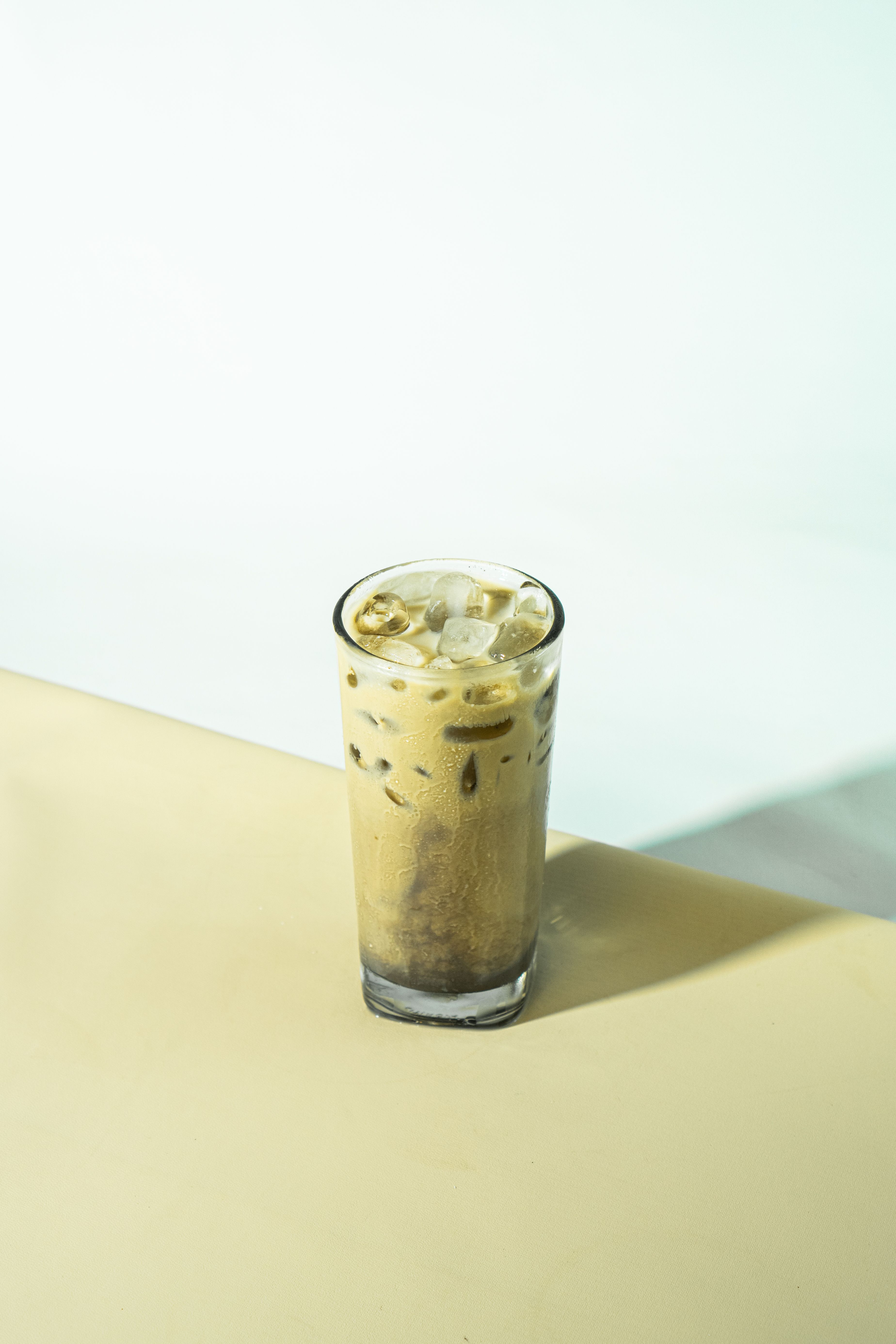 A tall glass of iced coffee with ice cubes on a soft, light background. Minimalist and refreshing.