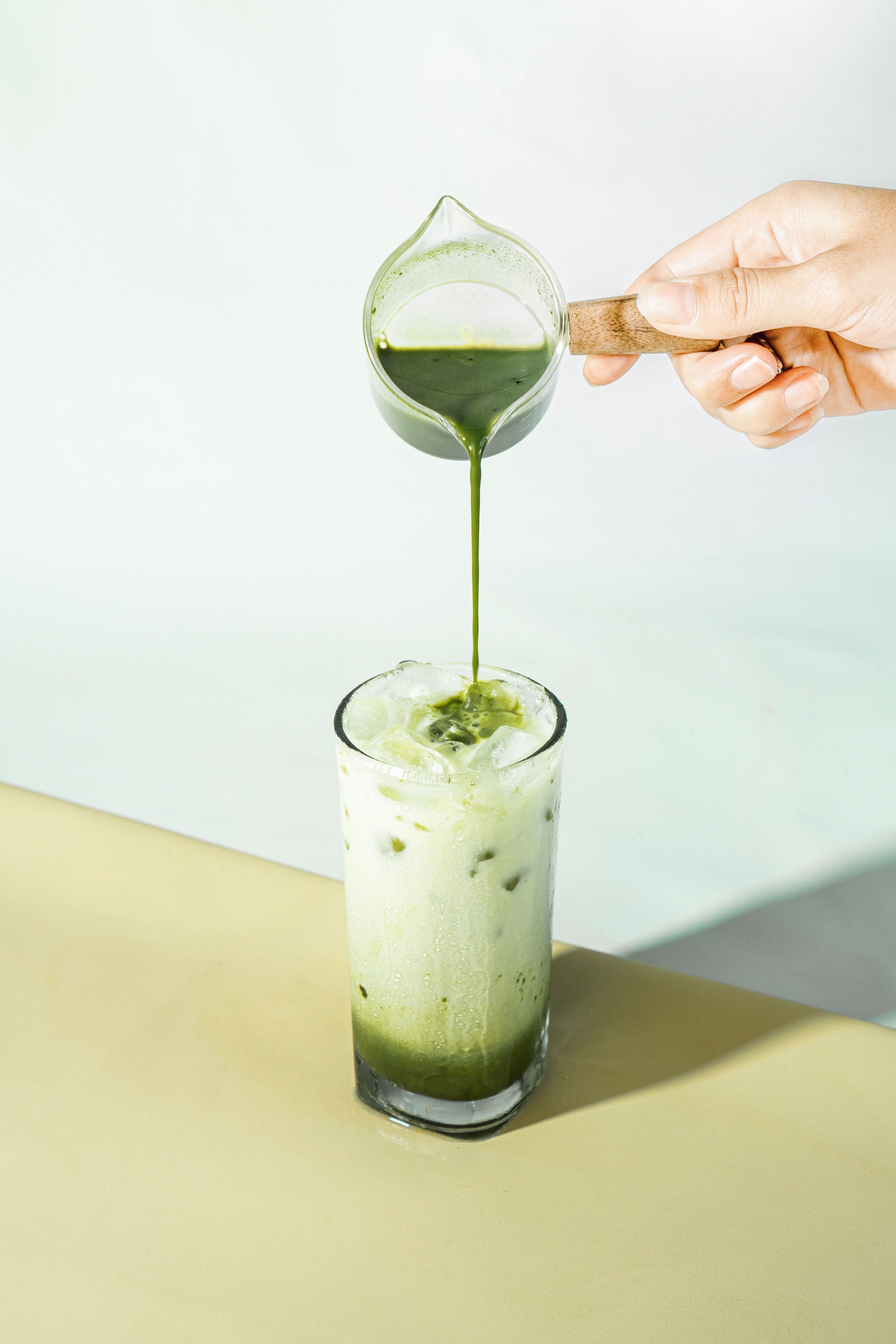 De franc Un refrescant cafè amb llet de matcha gelat que es serveix d'una gerra petita a un got alt sobre una superfície clara. Foto d'estoc
