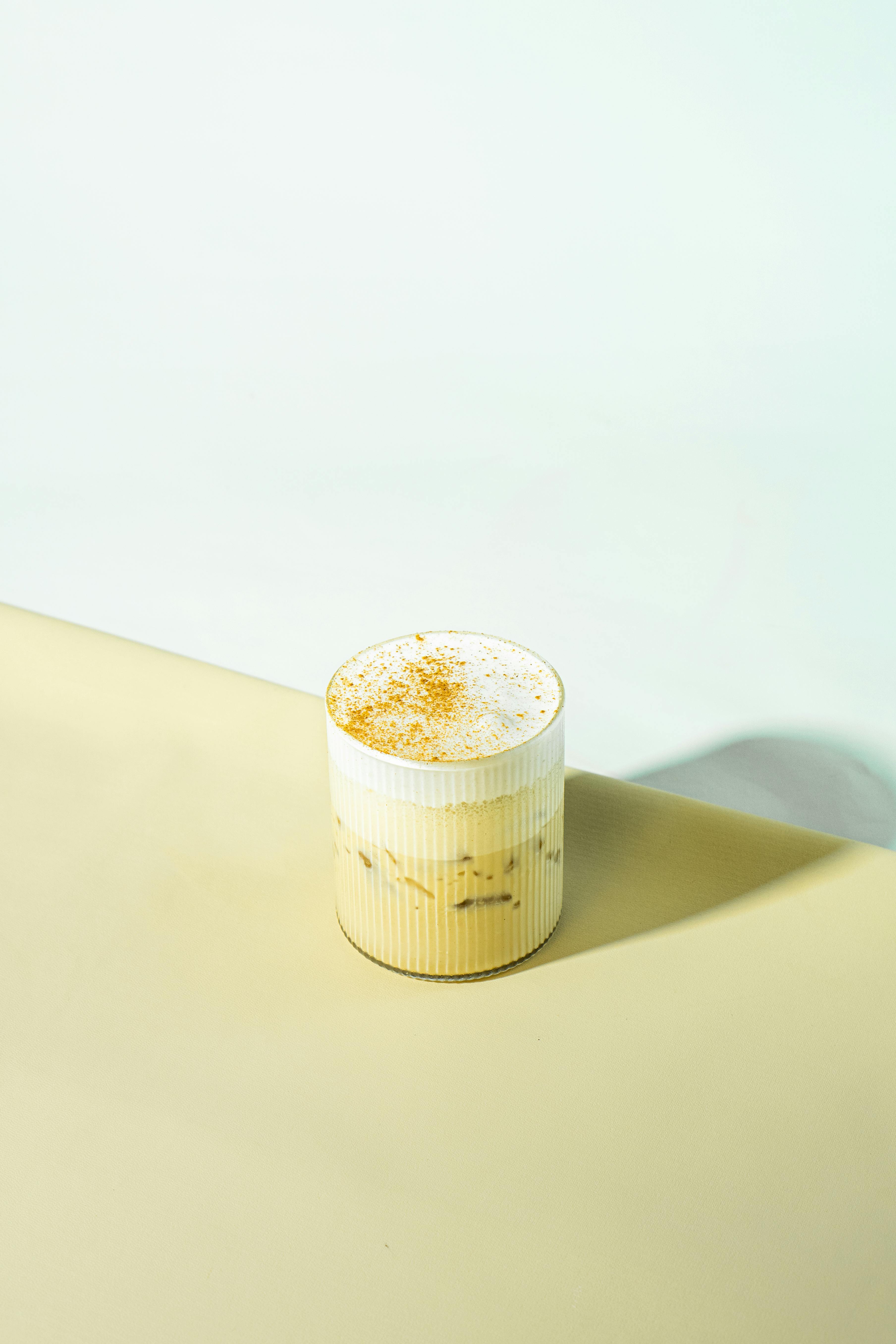 Aesthetic flat lay of a creamy iced coffee in a ribbed glass on a pastel background.