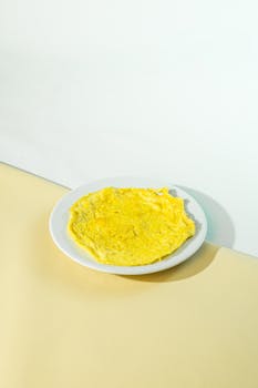 A bright yellow omelette on a white plate with a pastel background, perfect for breakfast inspiration.