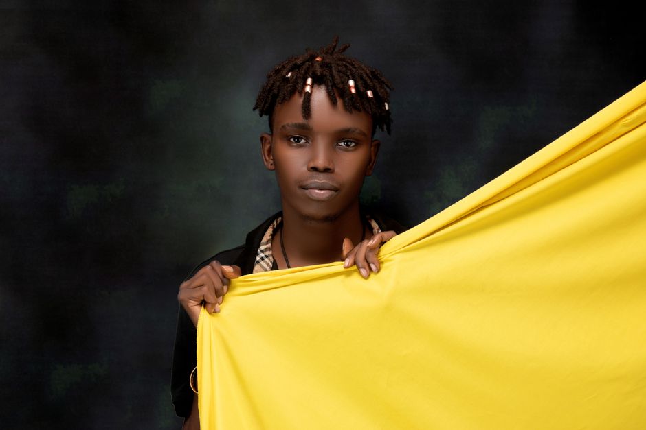 아이폰17 |모델·용량 선택 가이드 6 Portrait of a fashionable young man with unique hair holding a bright yellow fabric against a dark backdrop.