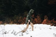 冬日，一名身着连帽外套的男子穿行于白雪皑皑的森林