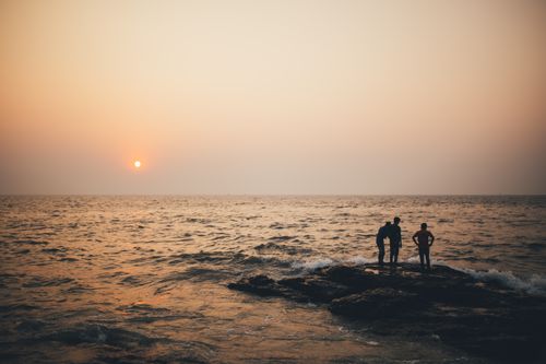 Free Captivating sunset view over the Arabian Sea in Mumbai, India, with silhouetted figures on the rocks. Stock Photo