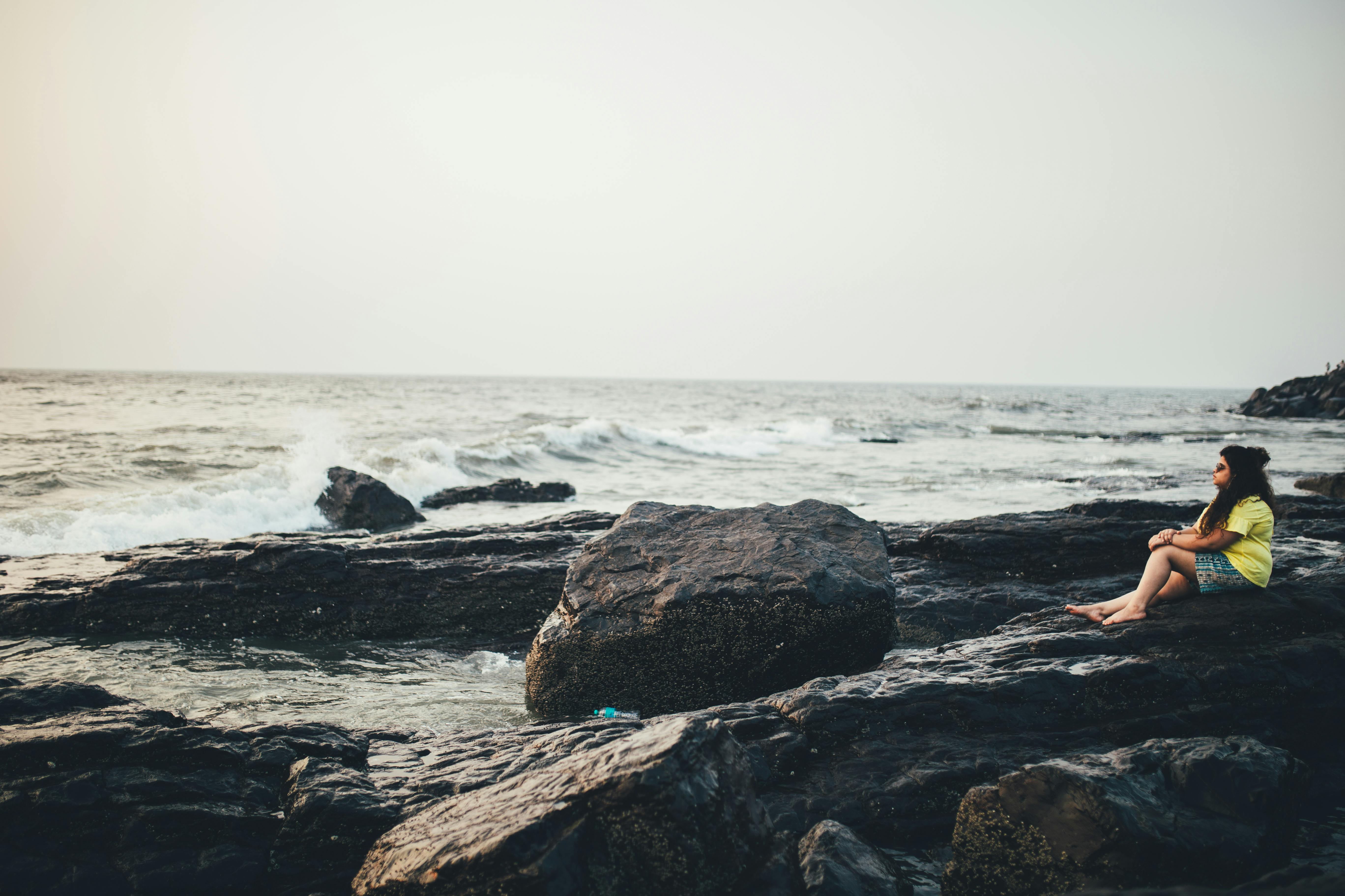 A woman relaxes on rocky shores of Mumbai, gazing at the ocean during sunset. Peaceful seascape scene.