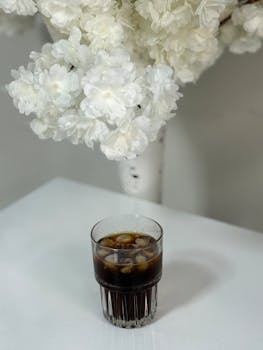 Glass of iced coffee with elegant white flowers in the background.