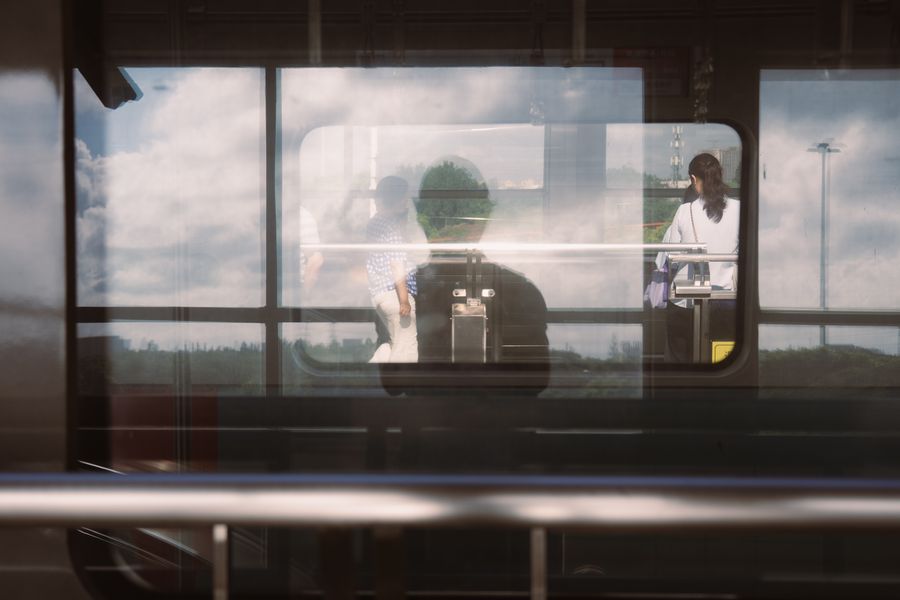 Reflection of passengers on a train window with a city landscape.