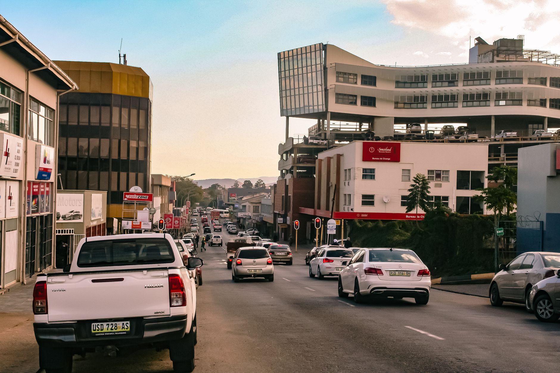 A bustling urban street in Manzini, Eswatini, showcasing modern architecture and evening traffic.