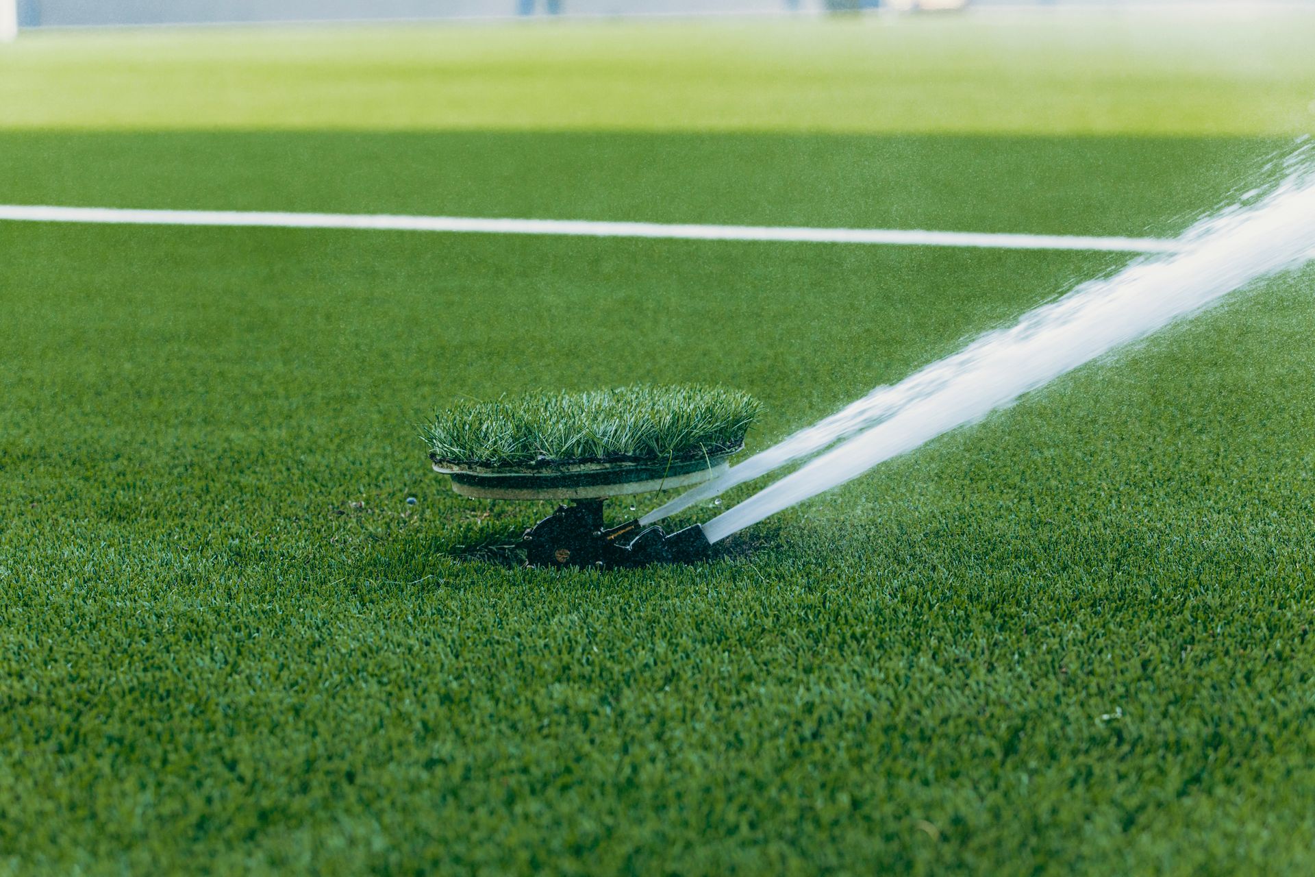 An active sprinkler watering a vibrant green sports field, enhancing the lush grass surface.