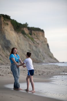 A heartwarming scene of a mother and son smiling and holding hands on a sandy beach at sunset.