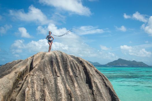 A woman in swimwear stands confidently on a rock with stunning ocean views in the background.