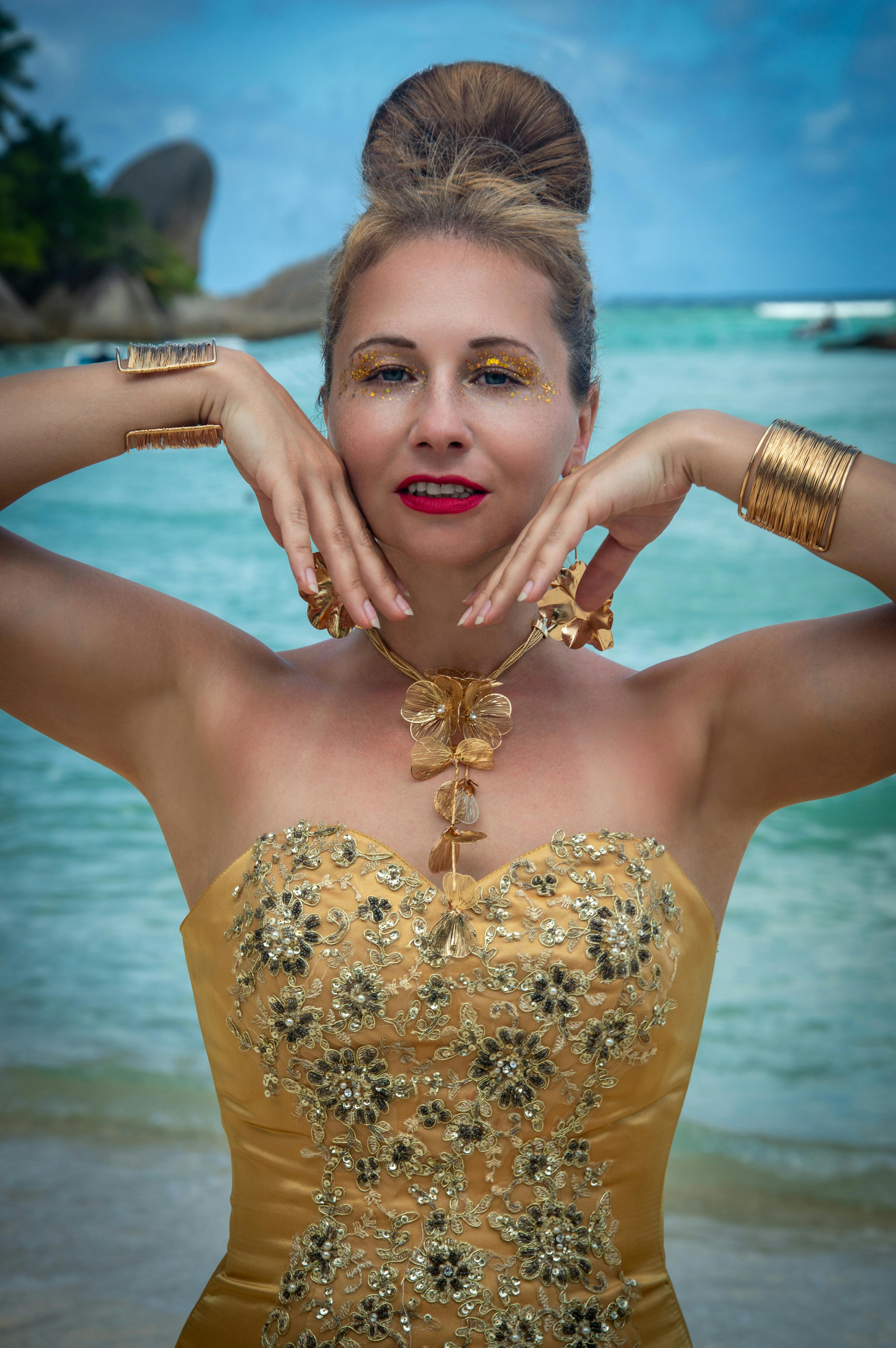 A stylish woman in gold attire striking a pose at a tropical beach, exuding elegance.