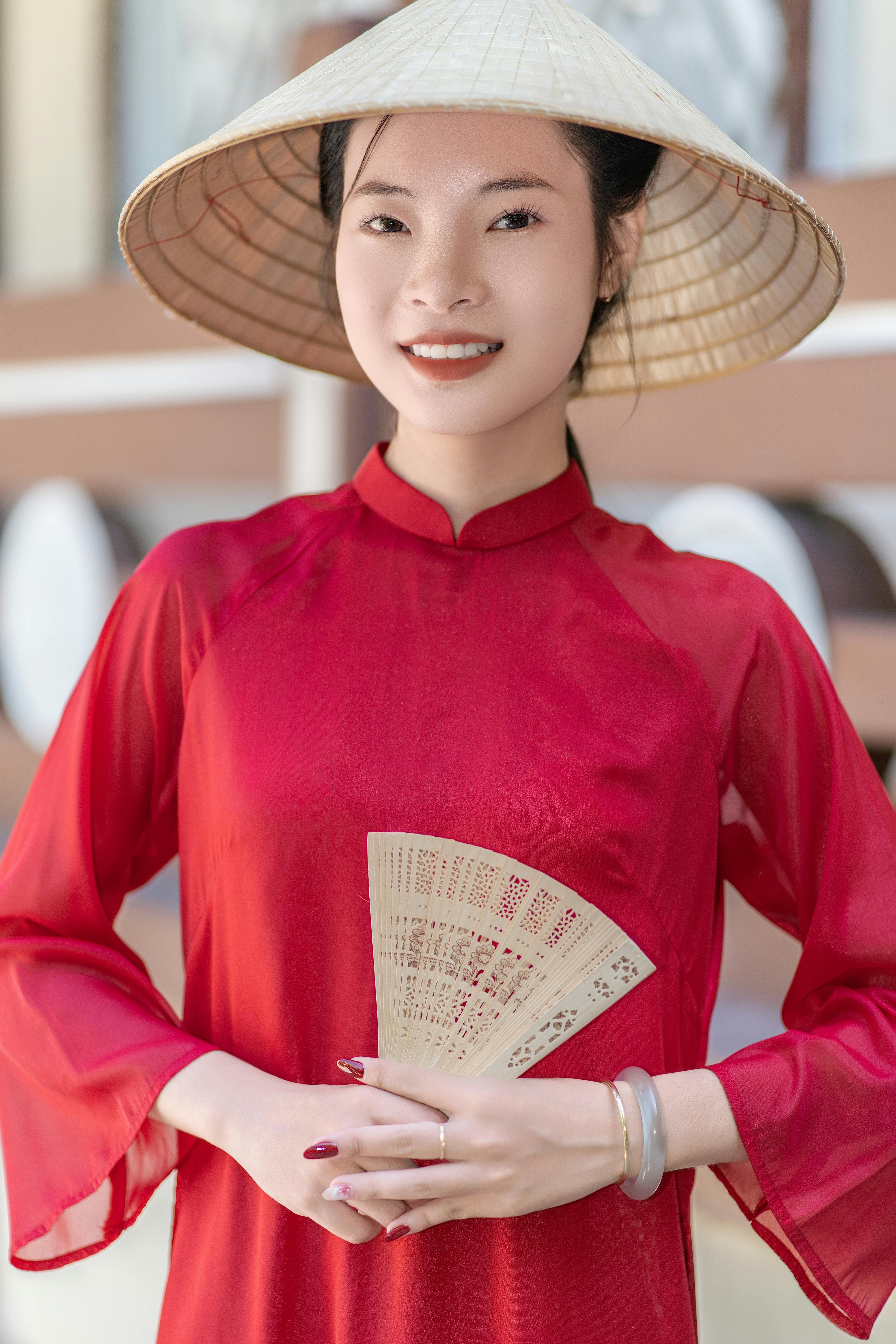 Portrait of a young woman in red ao dai with a conical hat and fan.