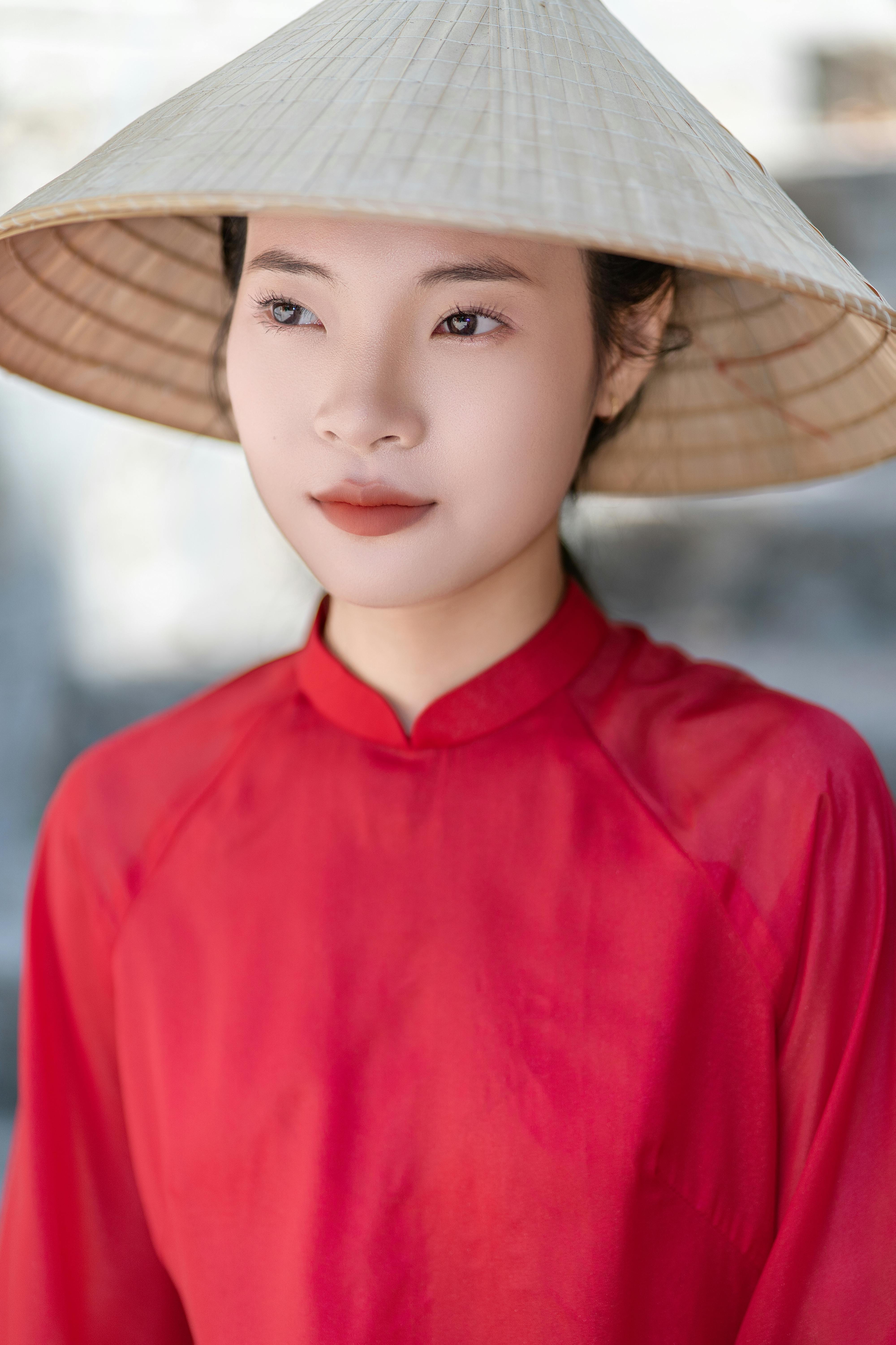 Young woman wearing a conical hat and red traditional dress in thought.