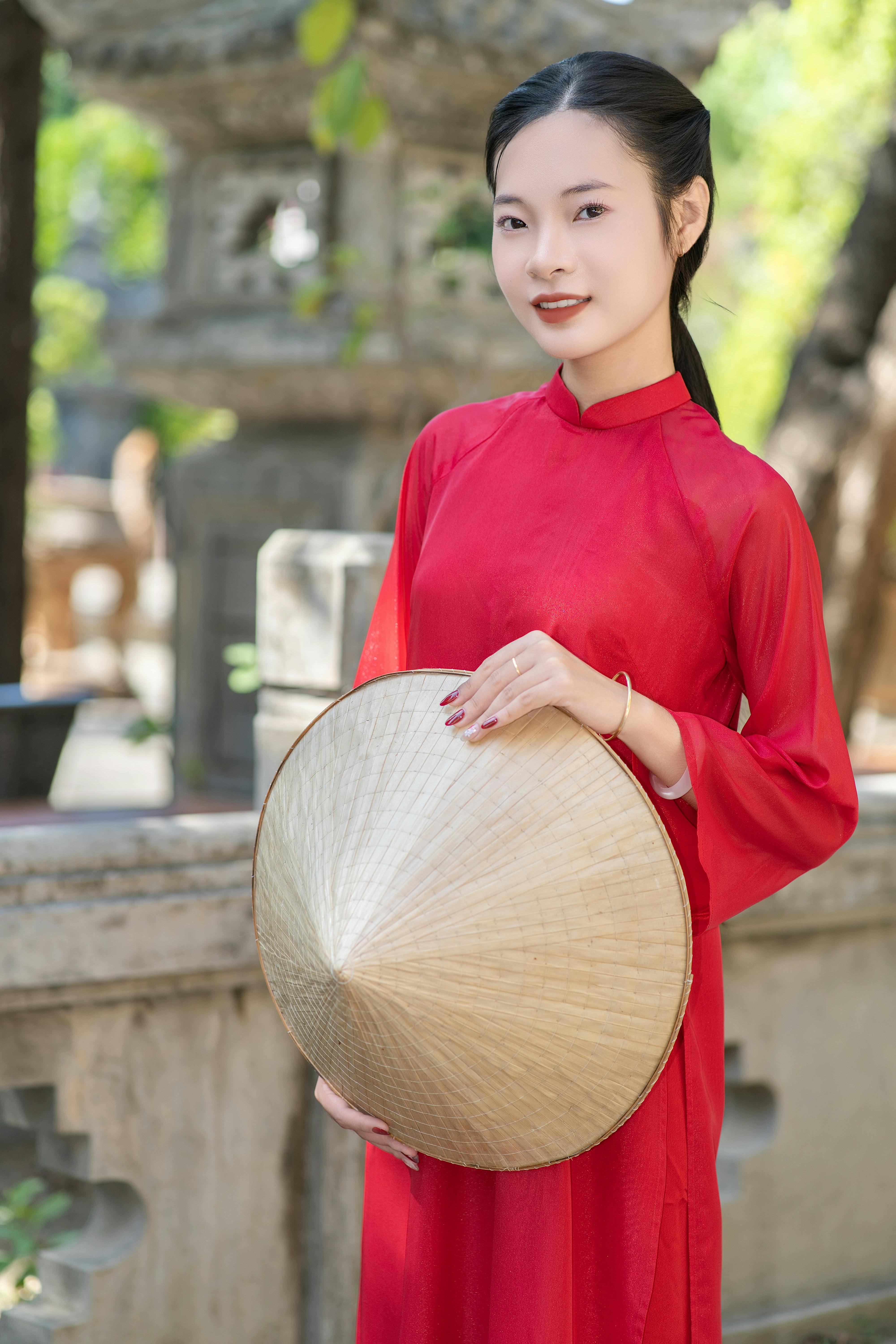 Woman in red áo dài with conical hat in serene outdoor setting