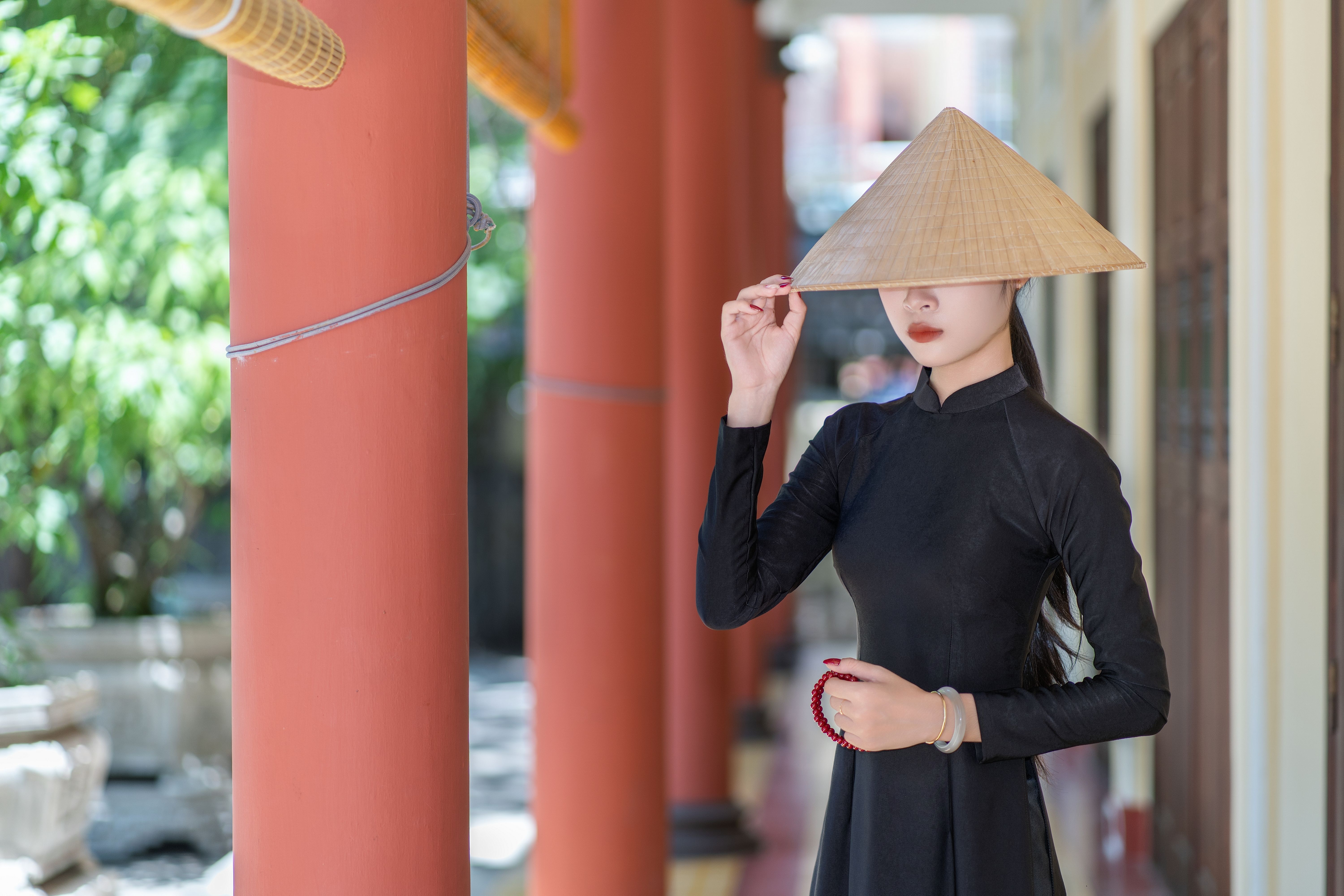 Young woman in traditional Vietnamese ao dai with conical hat in sunny outdoor setting.