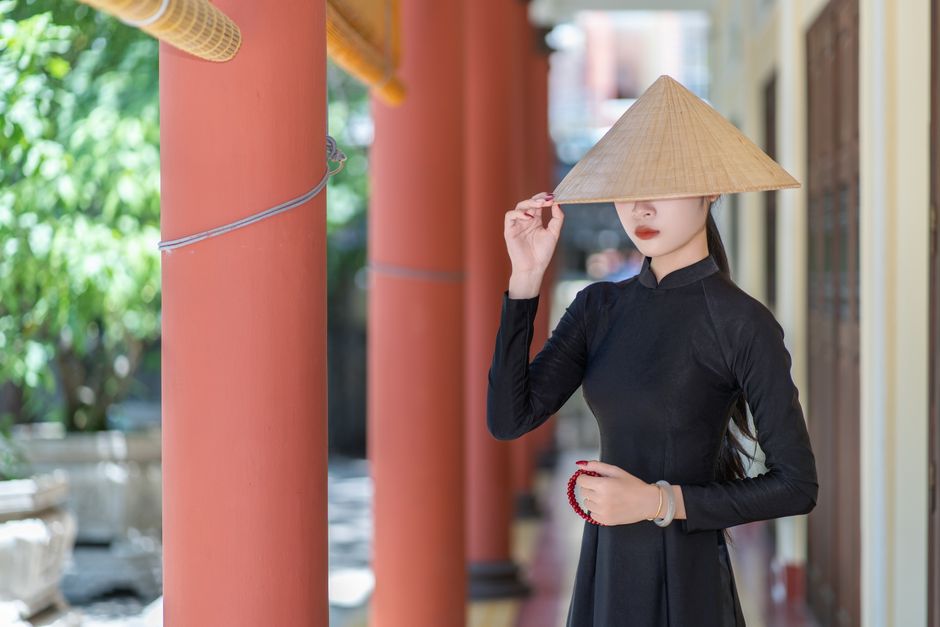 Young woman in traditional Vietnamese ao dai with conical hat in sunny outdoor setting.