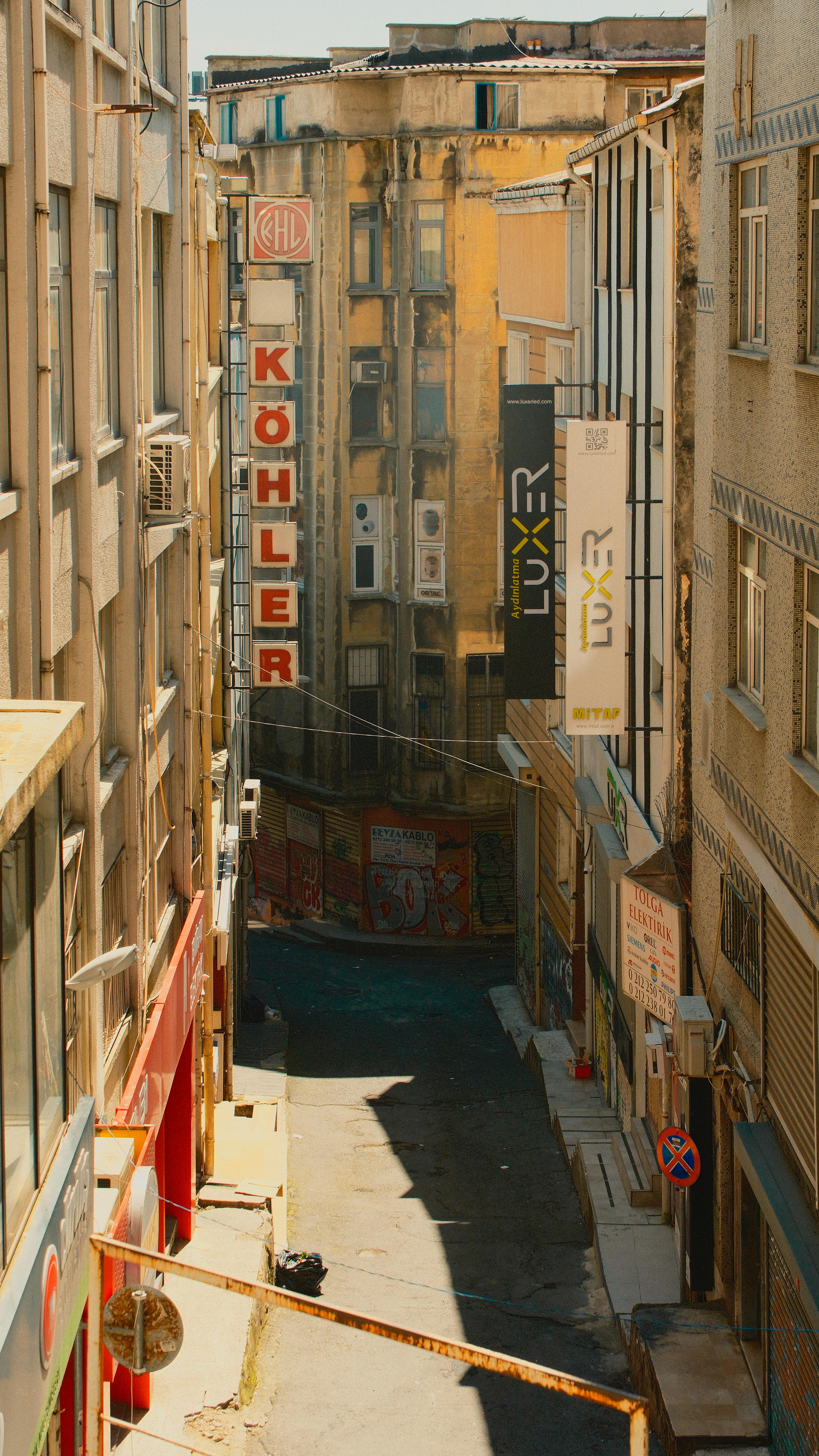 A narrow urban alleyway between tall, vintage buildings with signs and graffiti.