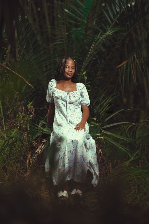 Free A woman in a floral dress sits amidst lush greenery, captured in a serene outdoor setting. Stock Photo