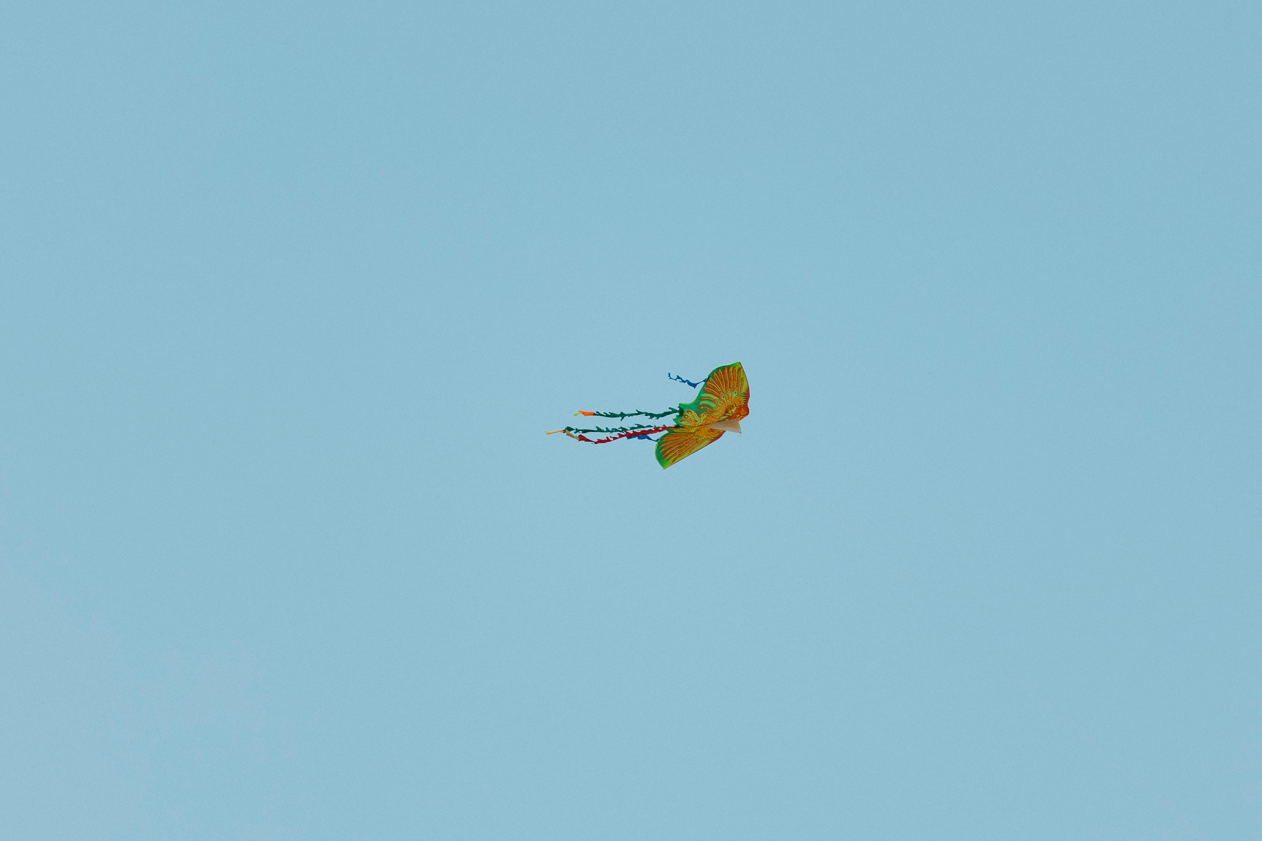 Kostenlos Ein bunter Drachen, der hoch in einem klaren blauen Himmel fliegt und Freiheit und Freizeit symbolisiert. Stock-Foto