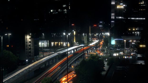 Night view of a bustling highway in Warsaw, Poland, featuring light trails and urban skyscrapers.