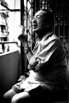 Black and white portrait of an elderly man smoking, captured in Ho Chi Minh City's urban setting.