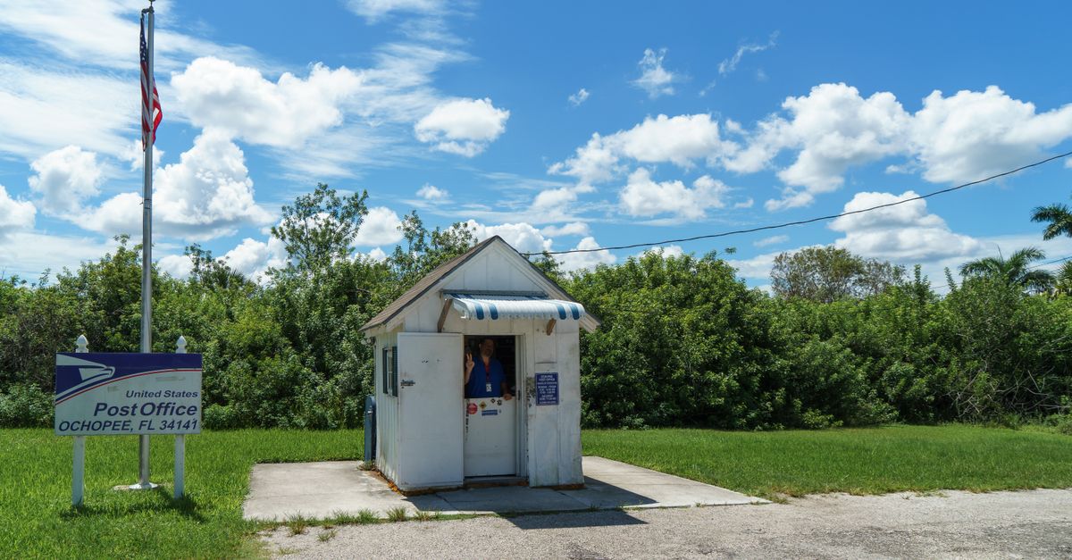 Ochopee's tiny Post Office with person and American flag in sunny setting.