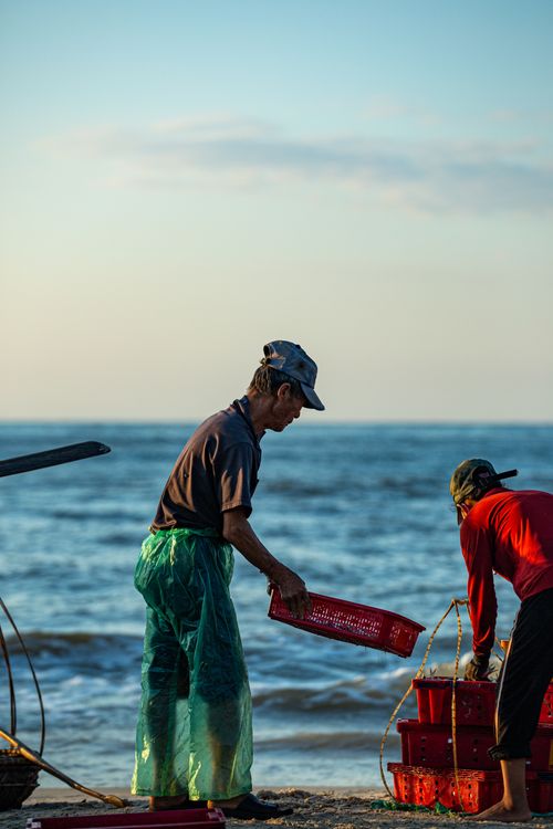 Free Two fishermen working with red baskets by the ocean during sunrise. Stock Photo