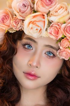 Close-up portrait of a woman wearing a pink rose crown, highlighting her blue eyes.