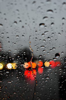 Raindrops on a window with colorful blurred street lights at night, creating a moody atmosphere.
