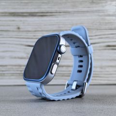 A smartwatch with a light blue strap standing on a wooden bench