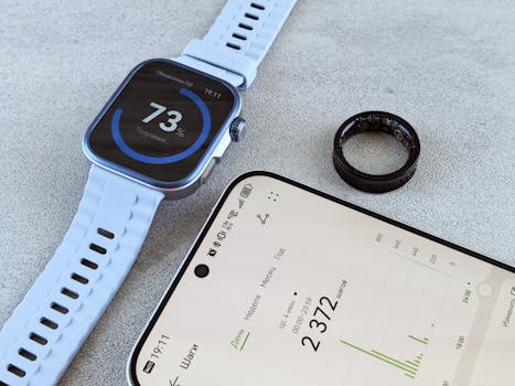 Smartwatch with fitness data, smartphone, and health ring on a gray surface.