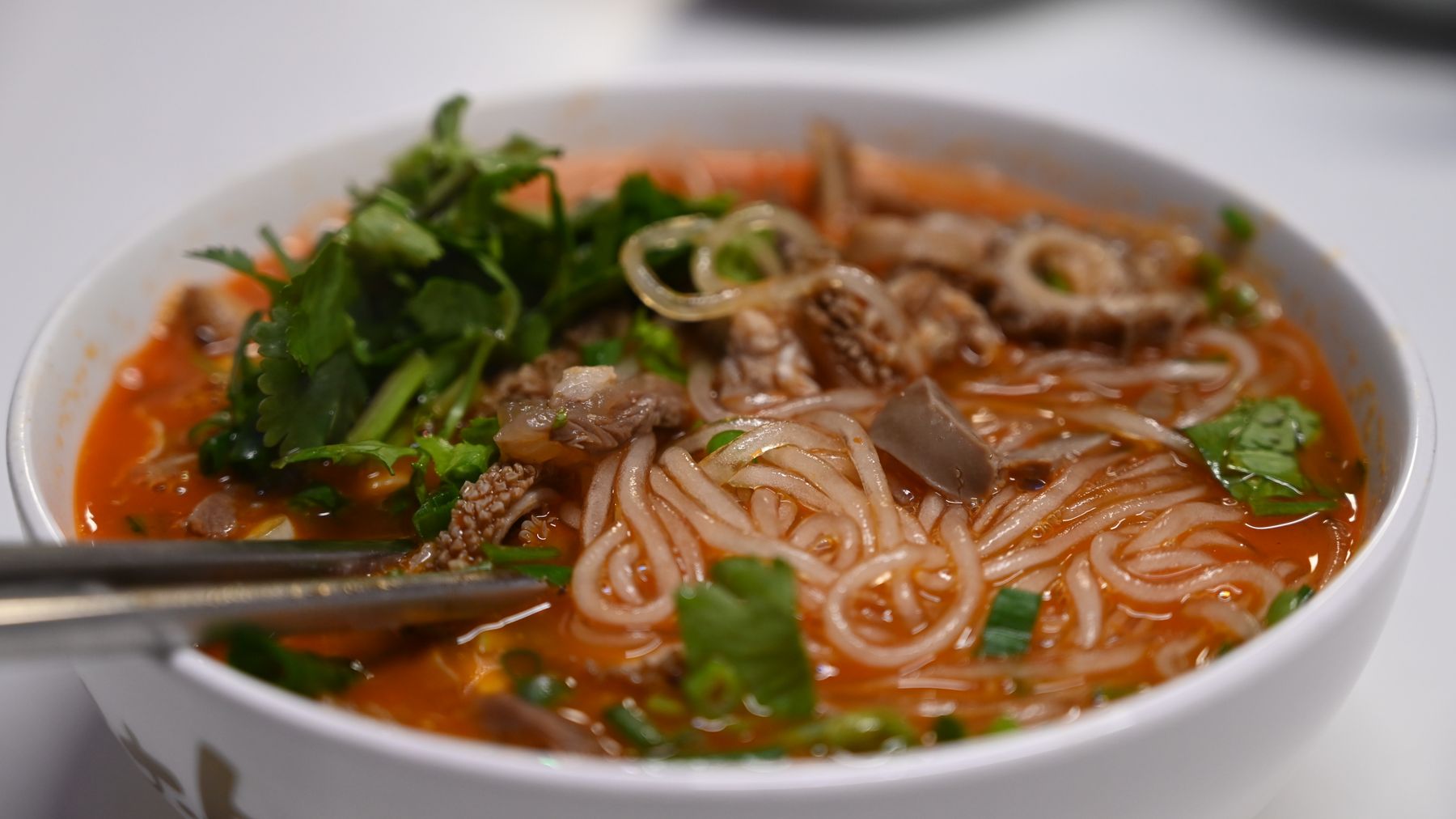 Close-up of a flavorful spicy noodle soup garnished with fresh cilantro and tripe.