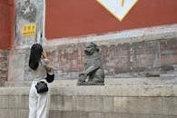 Woman Photographing Stone Lion Statue at Temple