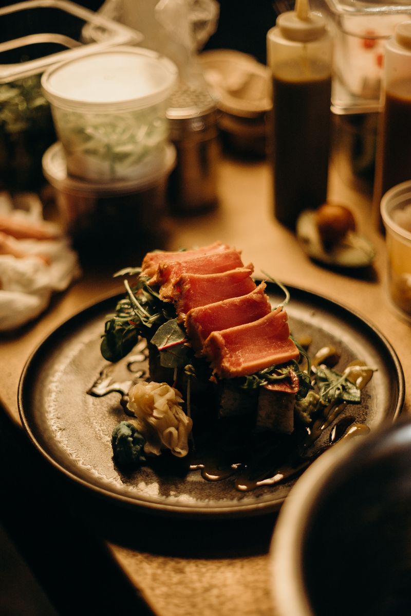 Seared bonito tataki on a dark plate — katsuo no tataki, the defining dish of Kochi, flame-charred with straw and eaten with garlic and ponzu