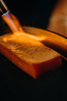 Close-up of a slice of tuna being torched for searing, emphasizing food preparation and culinary technique.