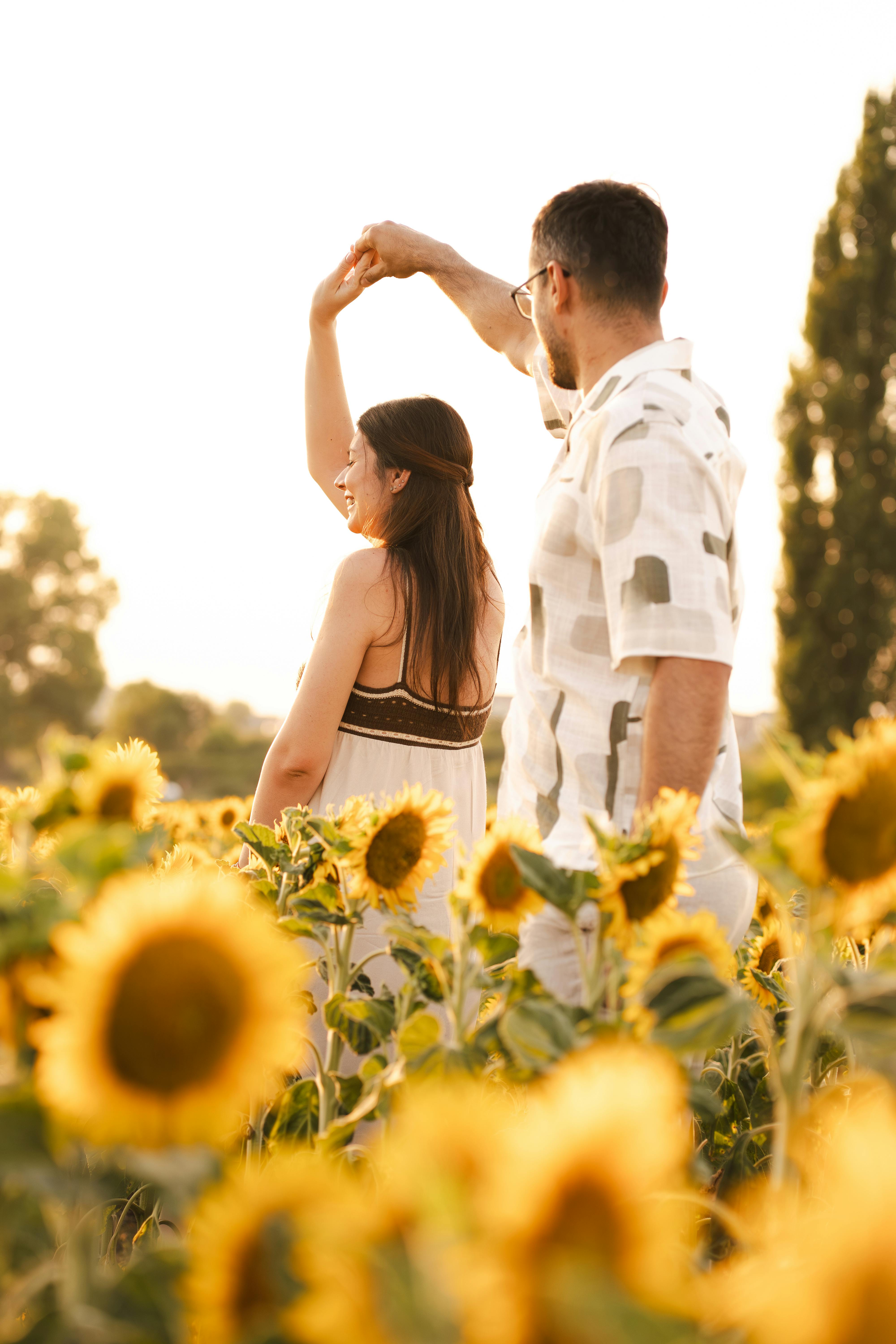 A loving couple dances amidst a vibrant sunflower field on a sunny summer day.