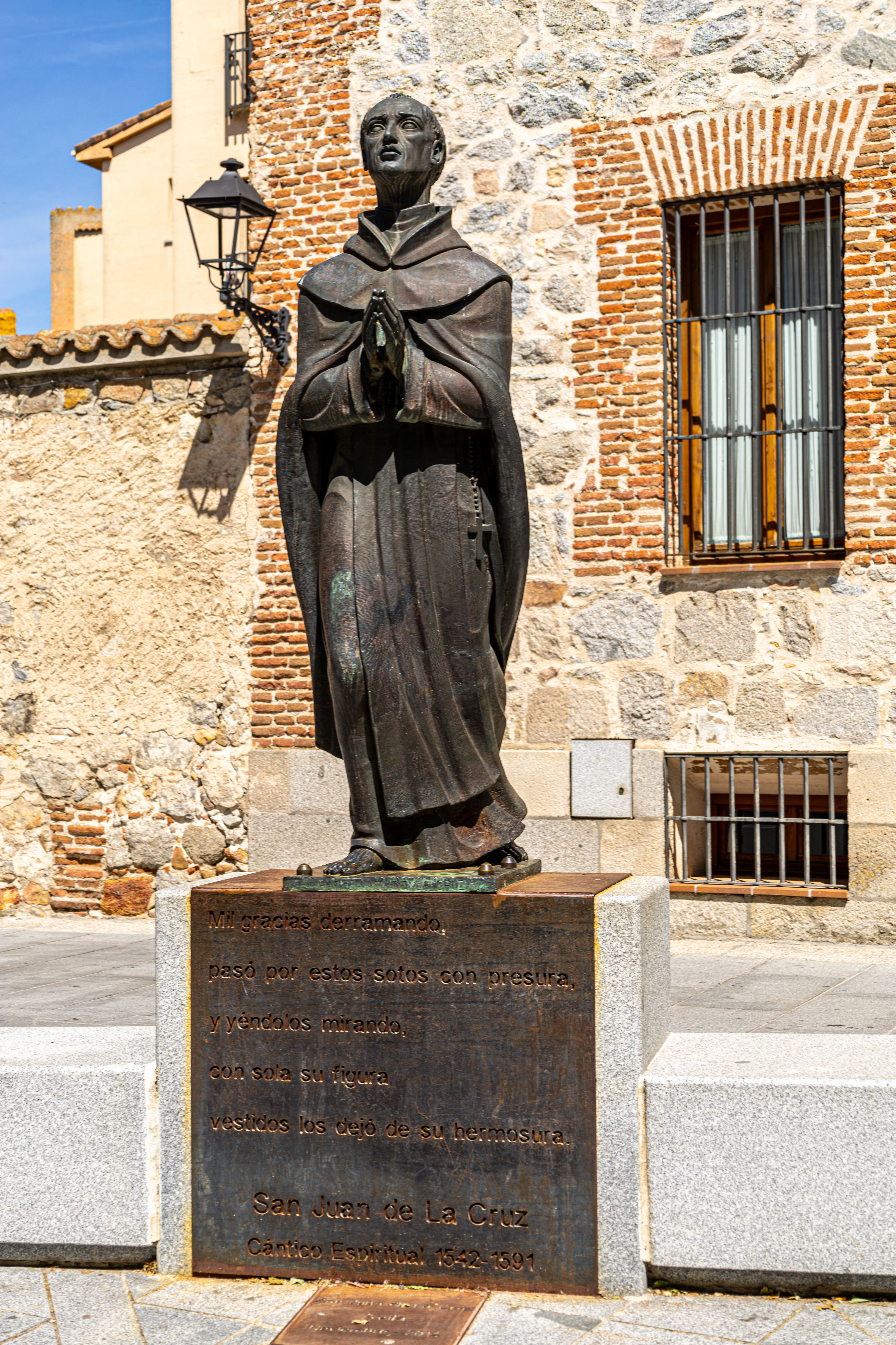 Bronze statue of San Juan de la Cruz at a historic brick wall in Ávila, Spain.