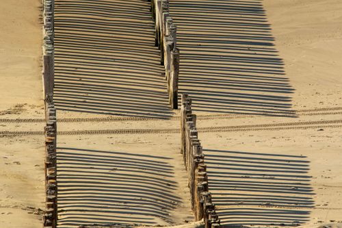 Free Wooden pilings casting dramatic shadows on sandy beach, creating a pattern. Stock Photo