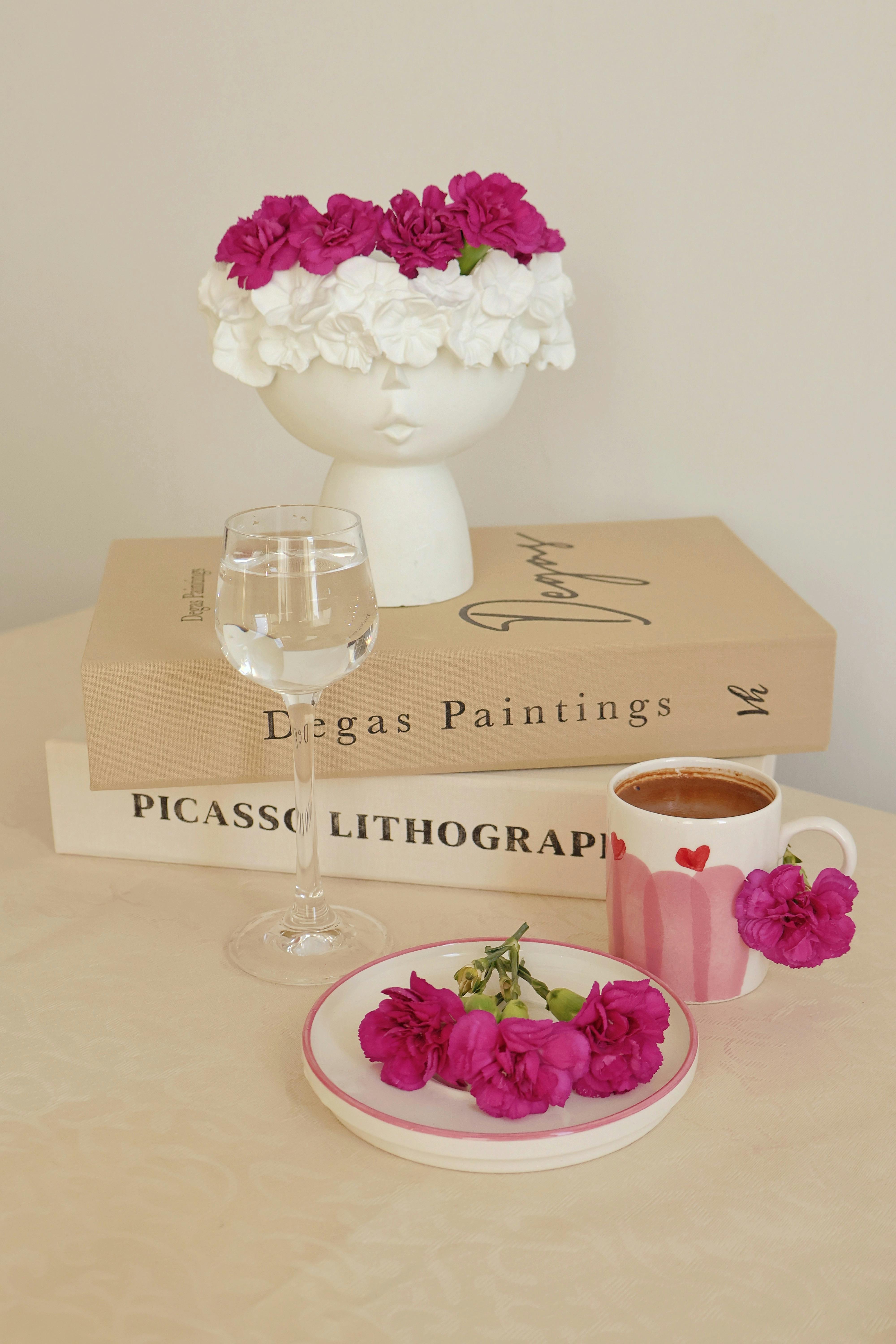 Artistic table with pink flowers, Degas and Picasso books, and coffee cup.