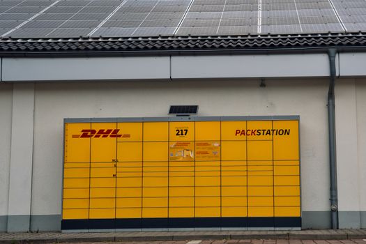 Yellow DHL Packstation under solar panels in Berlin, Germany, showcasing sustainable technology.
