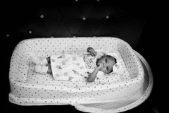 Adorable baby lying in a patterned crib, captured in elegant black and white.