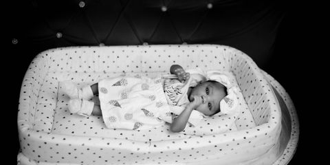 Adorable baby lying in a patterned crib, captured in elegant black and white.