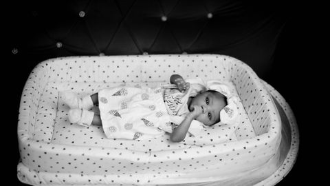 Adorable baby lying in a patterned crib, captured in elegant black and white.