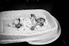 Charming black and white photo of a baby resting in a patterned bassinet.