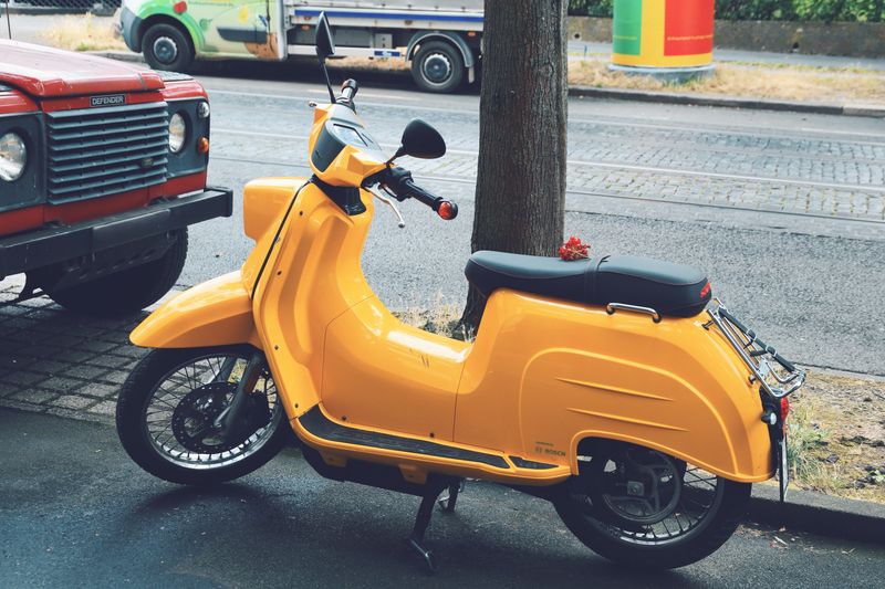 A bright yellow scooter parked on a city street next to vehicles, perfect for urban lifestyle imagery.