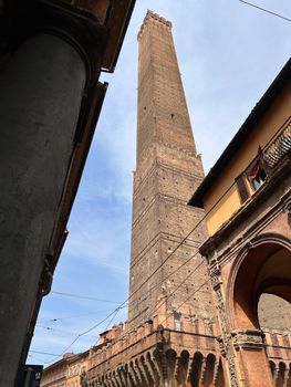 View of the historic Asinelli Tower in Bologna, Italy, framed by architectural details against a blue sky.