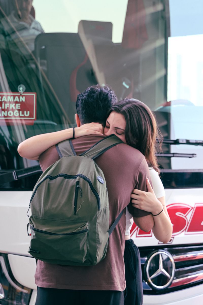 A heartfelt farewell between two people hugging near a bus station. Emotional goodbye.