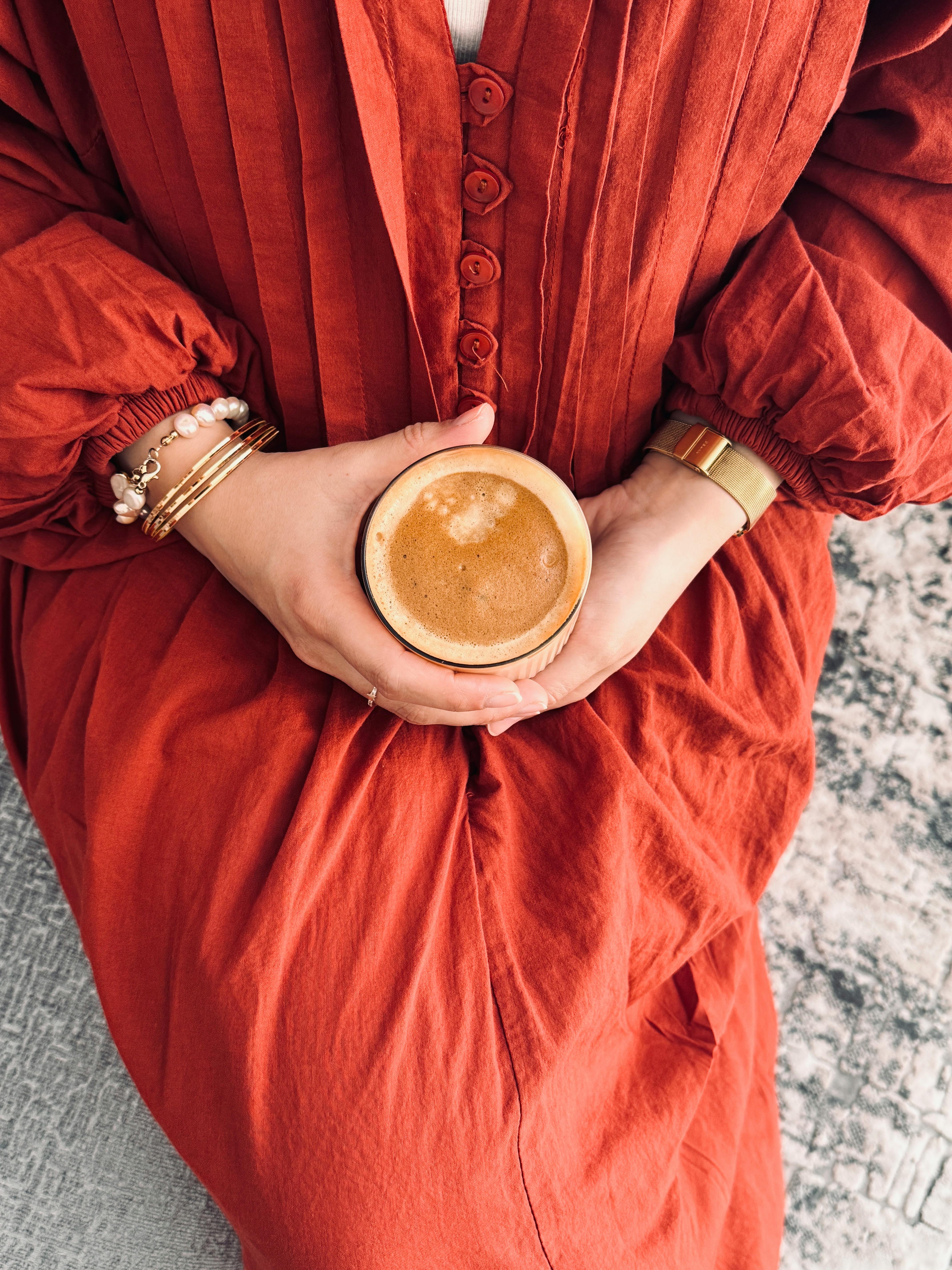 Top-down view of a person holding a coffee cup while wearing a vibrant orange dress. Cozy and warm setting.